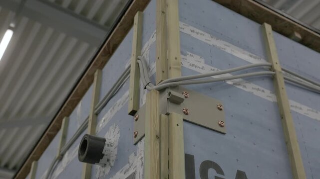 Factory-built wooden wall frame with insulation wrap, electrical conduit, and mounted junction box
