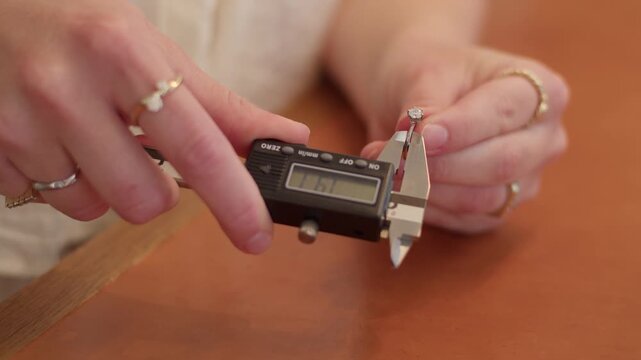 Jeweler using digital calipers to measure diamond ring size in workshop.