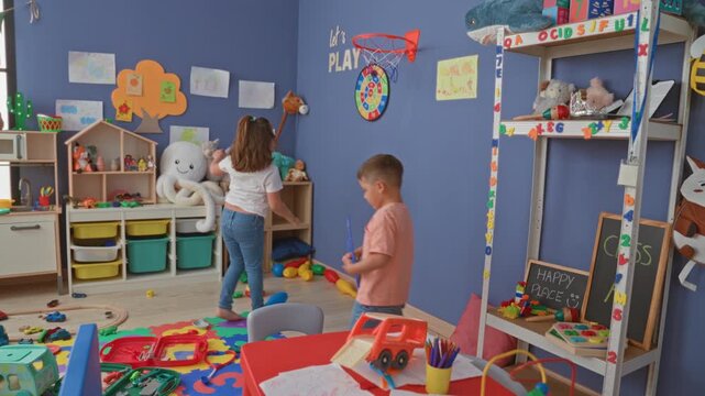 Hispanic boy and girl playing, girl reaching for stuffed toy and boy stacking blocks inside colorful playroom building; friendship creativity joy.