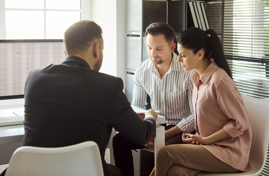 Couple and realtor meeting for mortgage consultation. A professional agent reviews contract paperwork with clients in modern office, discussing terms. Teamwork in real estate decision making.