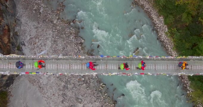 Everest region Nepal, top-down drone aerial shot of trekkers walking across the iconic Hillary Suspension Bridge above the rushing glacial waters of the Dudhkoshi River.