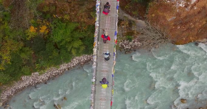 Everest, Nepal Top-down aerial shot shows hikers walking across the metal decking of the Hillary Suspension Bridge as the white rapids of the Dudh Koshi River flow underneath.