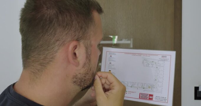 Man reading the emergency evacuation plan posted in a hotel room. Travel concept of hotel safety, fire evacuation, emergency preparedness, and guest information.