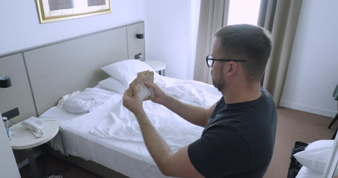 Man counting cash in a hotel room while calculating accommodation expenses. Travel concept of hotel costs, budgeting, business travel, overnight stay, and expense management.