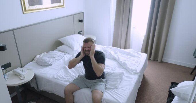 Man sitting on a hotel bed feeling sick during his vacation. Travel concept of illness, flu, discomfort, recovery, and disrupted holiday plans.