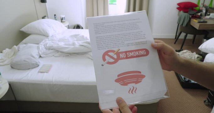 Person holding a no smoking policy document inside a hotel room. Travel concept of smoke-free accommodation, hotel regulations, guest information, and safety rules.