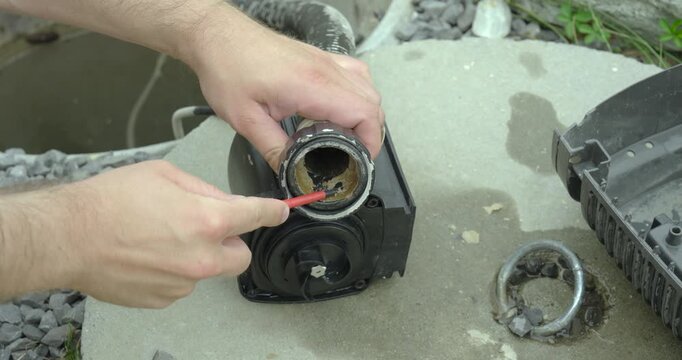 Close-up of a person scraping limescale deposits from a pump housing using a screwdriver during maintenance. Concept of descaling, repair, cleaning, and mechanical servicing.