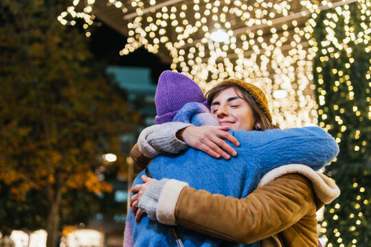 Friends hugging celebrating winter holidays with lights