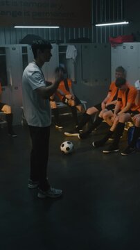 Coach Stands Before Group of Exhausted Teenage Football Players in Locker Room. Man Gestures, Expressing Disappointment and Critiquing Performance After Defeat. Youth Sports Discipline. Vertical Shot.