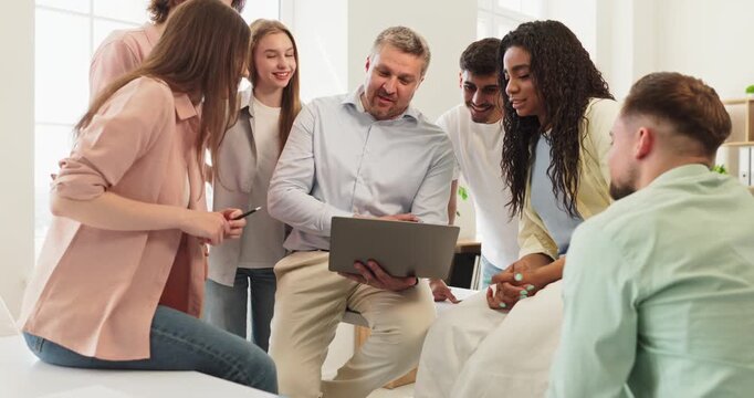 Teacher and students discuss lesson using classroom laptop. The professor guides a group discussion and reviews key concepts for clarity. Clear concept of collaborative education and teamwork.