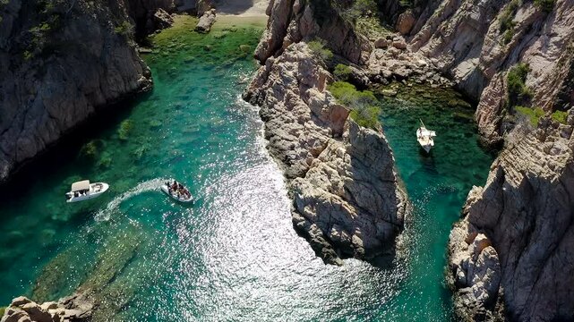 Aerial view of Cala Marquesa with boats, featuring spectacular rocky cliffs, narrow sea fissures, rugged islets and the crystal-clear Mediterranean waters of the Costa Brava. 