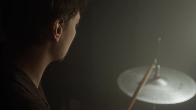 Caucasian young man adjusting hi-hat clutch and playing perforated cymbal with drumsticks in studio. Footage for music school promos or instrument retail advertisements