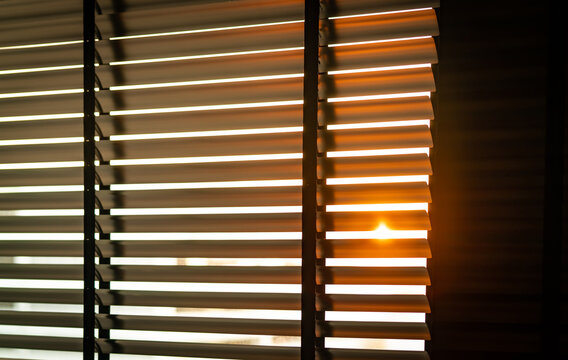 Opened venetian plastic blinds with morning sunlight streaming through a residential window. Modern living room design, privacy. Horizontal slatted shades, minimalist interior design, privacy control.