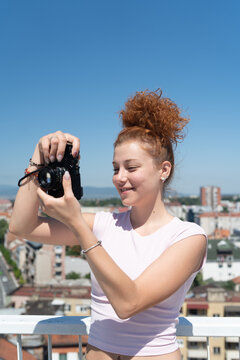 Young redhead woman photographer phototographing city from a building rooftop on a sunny summer day