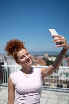 Beautiful and young redhead woman taking a selfie with a mobile phone on the rooftop of the city building