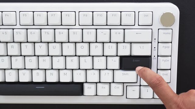 View of a finger pressing the Enter key on a black and white mechanical keyboard.