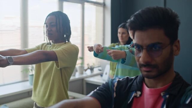 Multiethnic young adult colleagues performing wrist stretching exercises together in contemporary office. Ideal for corporate wellness programs and healthy workplace culture campaigns