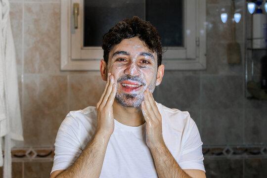 Young man enjoying daily self-care routine with face wash in bathroom