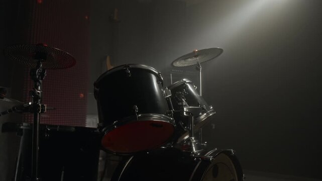 Drum kit standing on dark stage under bright spotlight in hazy music studio. Professional musical equipment for concert promos or music academy advertisements