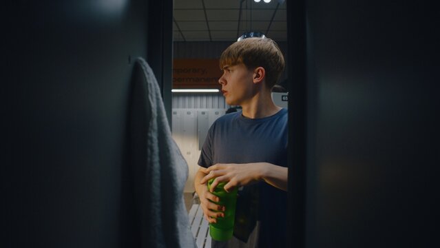 Inside Gym Locker Young Male Athlete Opens Door. Boys Places Black Sports Bag Inside Compartment, Grabs Water Bottle, and Takes Sip Before Heading Out. Realistic Athletic Preparation Routine.