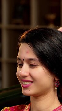 Indian Asian mother in her fifties lovingly giving an oil head massage to her pretty young daughter while sitting together on a sofa at home, expressing care and affection