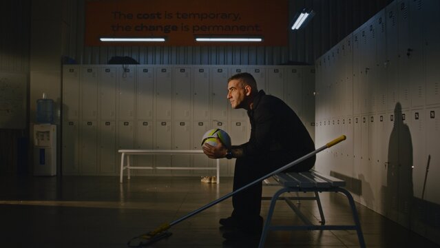 Tired Cleaner in Takes Break From Mopping Sports Locker Room. Man Sits on Bench, Picks Up Soccer Ball Left Behind by Team, and Holds it With Both Hands, Contemplates Youth With Sense of Nostalgia.