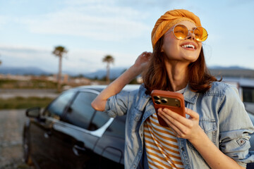 Naklejka premium woman lifestyle outdoor sunny smiling smartphone denim jacket fashion casual portrait mood as she relaxes beside a car enjoying a bright day and free spirited vibe