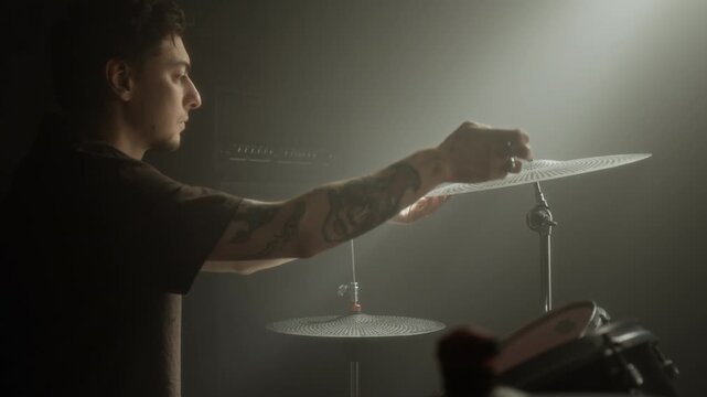Young Caucasian man adjusting cymbal on drum kit and playing with drumsticks in music studio. Footage for music education videos or musical instrument marketing campaigns
