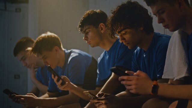 Youth Boys in Sports Uniforms Sitting on Locker Room Bench. Teenager Absorbed in Own Mobile Phone, Scrolling Through Social Media or Apps Before Training. Modern Technology Addiction, Screen Time.