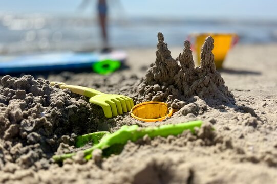 A charming sandcastle construction on a sunny beach, surrounded by colorful plastic toys like rakes and buckets. A nostalgic scene capturing summer fun, seaside play, and childhood imagination.