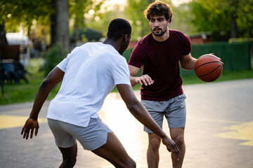 Fototapeta premium Young men playing competitive street basketball outdoors