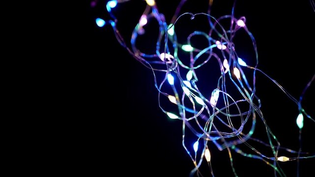 Thin tangled strings of colorful LED fairy lights twinkle against a pitch black background. Concept of festive holiday celebrations, magical moments, and party decoration.