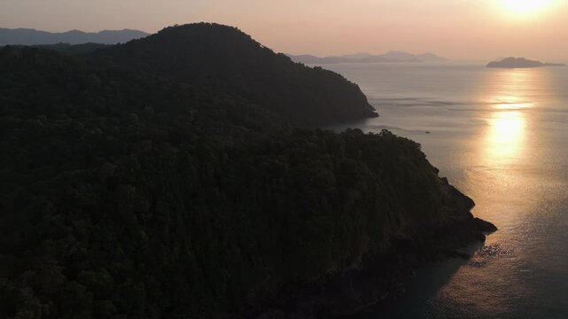 Low aerial drone shot skimming the palm tree tops along Wai Chek Beach in Koh Chang, featuring a beautiful sunrise and silouetted coastline