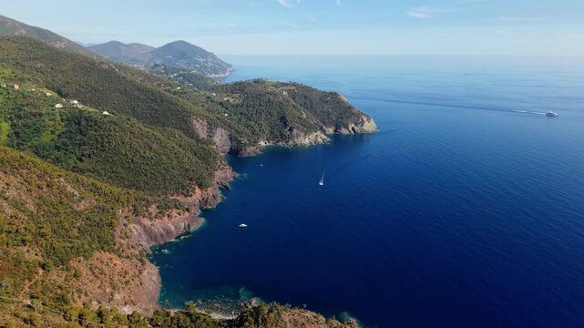 Drone footage shows rugged Italian coastline with green hills and boats on blue sea