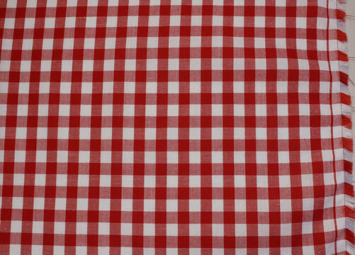 Texture of classic red plaid cotton cloth with fringed edge. Close up of red and white gingham fabric background.	