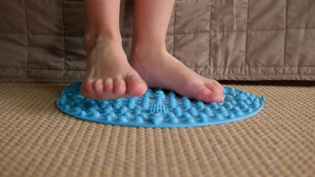 Person walking on acupressure foot massage mat. Close-up of bare feet doing therapeutic exercises on a spiky mat to stimulate reflexology points, preventing flat feet and promoting blood circulation
