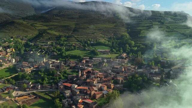 Aerial view of mountain village in Catalonia surrounded by green hills and morning clouds in the Pyrenees