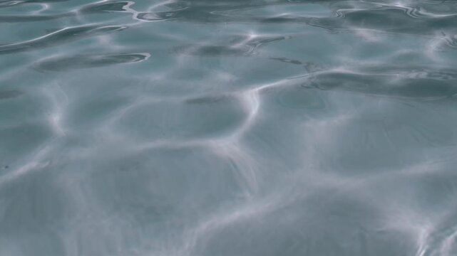 Bright sunlight creates dancing caustic patterns on the gently rippling surface of clear blue water. Concept of summer vacation, refreshing relaxation, pure environment, and peaceful travel.