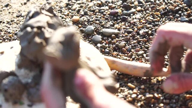 Clay sculpture hands shaping small cat figure outdoors on sunny day