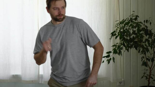 Energetic adult Caucasian man dancing dynamically in a bright bedroom. Active male enjoying morning fitness routine, moving fast with motion blur, having fun, exercising, and feeling free at home.