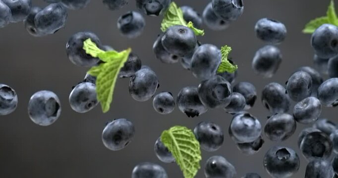 Blueberries with mint leaves falling in super slow motion on black background