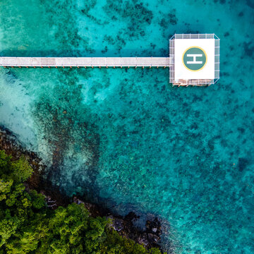 Aerial view of helipad over the sea. Helicopter parking platform station linked to the land by long concrete bridge over turquoise water of Andaman sea at Nyaung Oo Phee island in Myanmar or Burma.