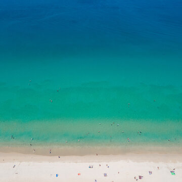 Aerial top view of summer activities on tropical beach landscape at Surin beach in Phuket, Thailand. Turquoise waves reach the coast while tourists sunbathing, swimming and relaxing on vacation travel