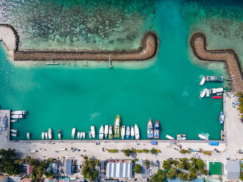 Aerial top view of Maafushi island jetty with tour boats parking inside the breakwaters. Nautical vessel transportation system for Maldives travel industry