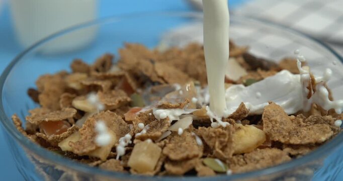Fresh milk pouring into crispy cereal flakes in white bowl in ultra slow motion