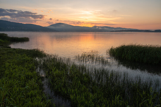 Sunrise Over Peaceful Lake With Reeds and Mountains