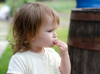 Portrait of a thoughtful toddler girl in a rustic setting. Close-up profile portrait of a little girl looking thoughtful while eating outdoors, with a classic rustic wooden barrel in the  © Svitlana Dvuilo