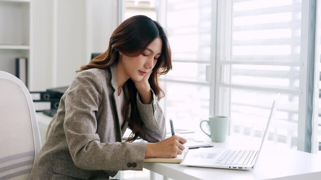 Young businesswoman hand holding pen taking notes , sitting at desk with laptop , analyzing information.