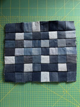 Rectangular denim patchwork in progress made from recycled jeans in various shades of blue and grey, handmade textile art on green cutting mat 