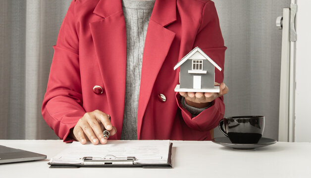 The real estate agent explains the business contract, holding a model house, a sign for rent, and insurance